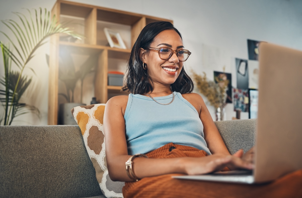 Laptop, young woman and working from home with a smile writing for website.