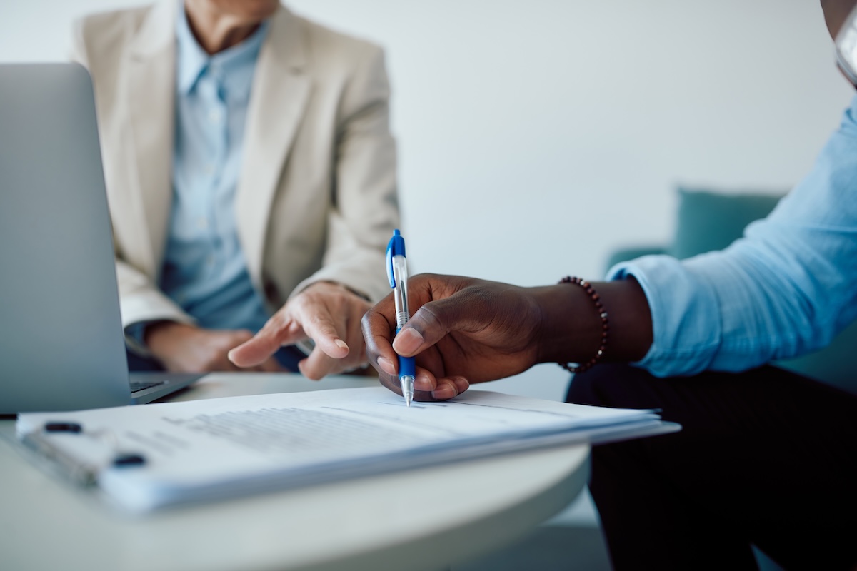 Close-up of a man signing contract with insurance agent in the office.